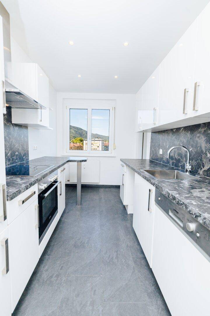 Moderne Küche mit weißen Hochglanzfronten, dunklen Arbeitsplatten und Fenster mit Bergblick.