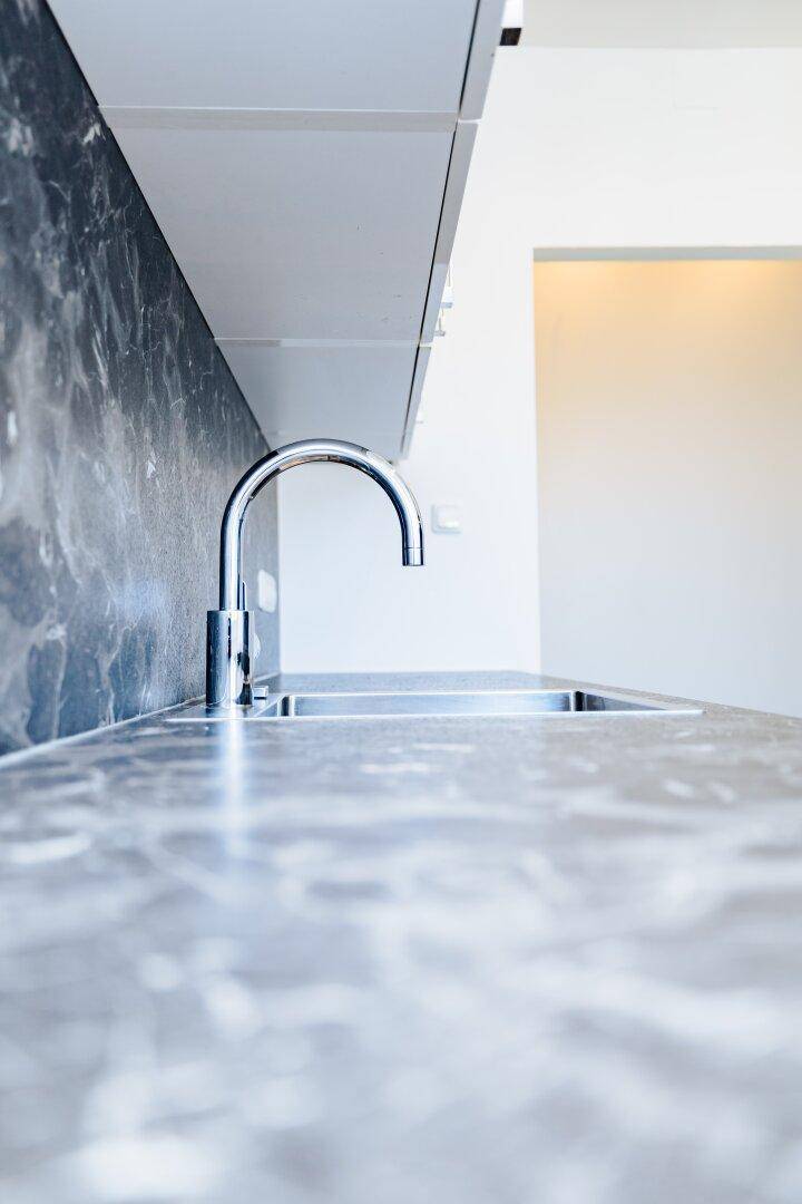 Detailaufnahme der Küchenspüle mit modernem Wasserhahn und dunkler, gemusterter Arbeitsplatte.