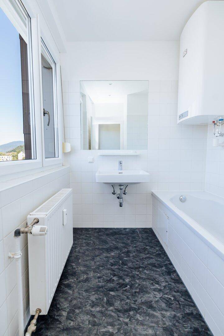 Helles Badezimmer mit Badewanne, Waschbecken, Fenster und Blick auf die umliegende Landschaft.