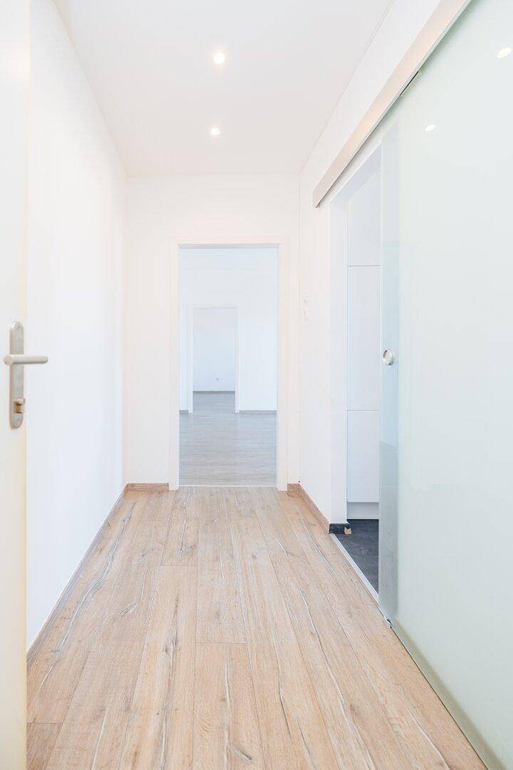 Heller Flur mit modernem Laminatboden und einer eleganten Glasschiebetür.