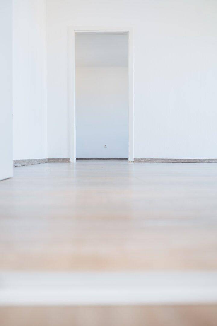 Detailaufnahme des hellen Laminatbodens und eines Türrahmens in einem leeren Raum.