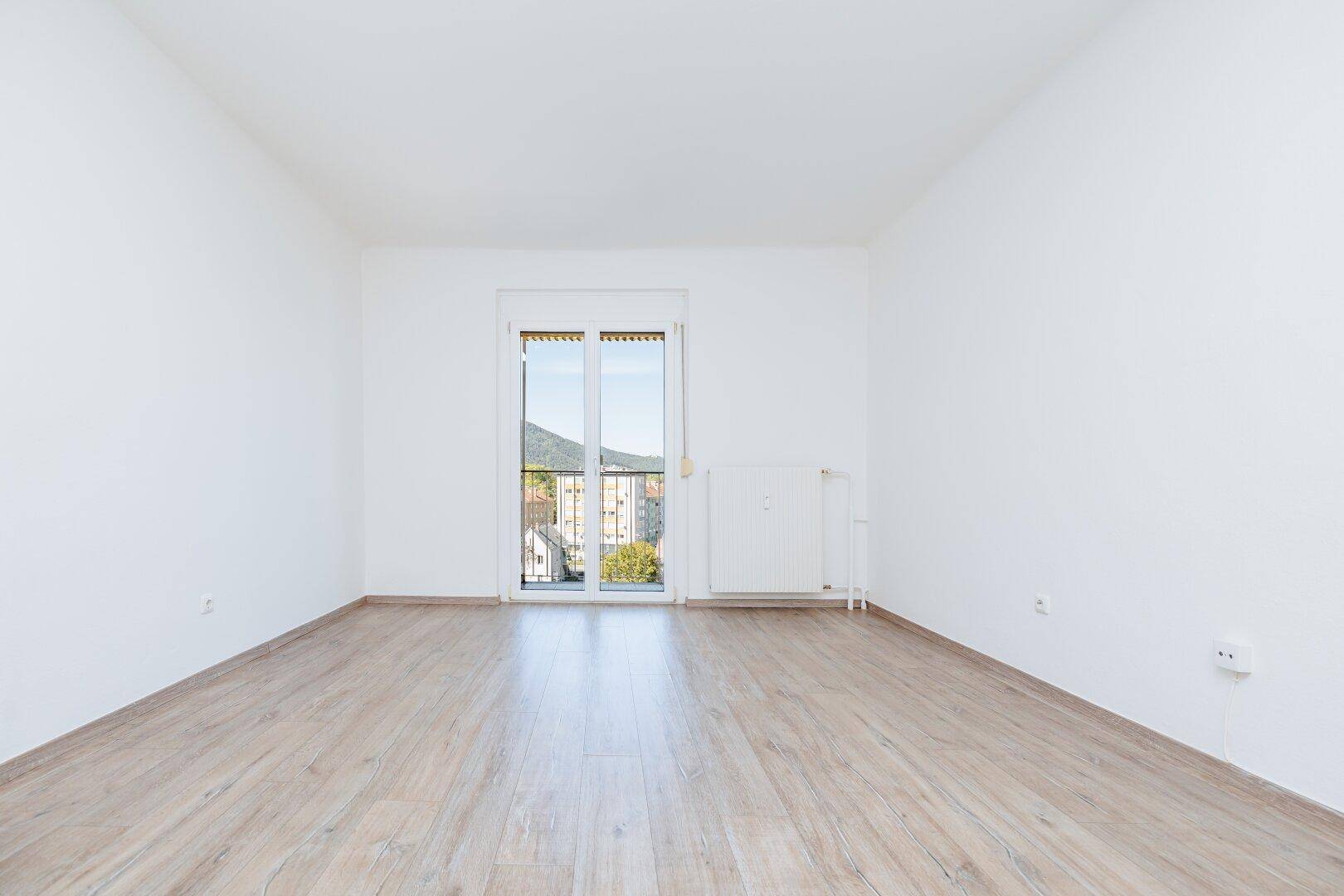 Geräumiges Zimmer mit hellem Laminatboden und Balkonzugang, bietet einen weiten Blick.