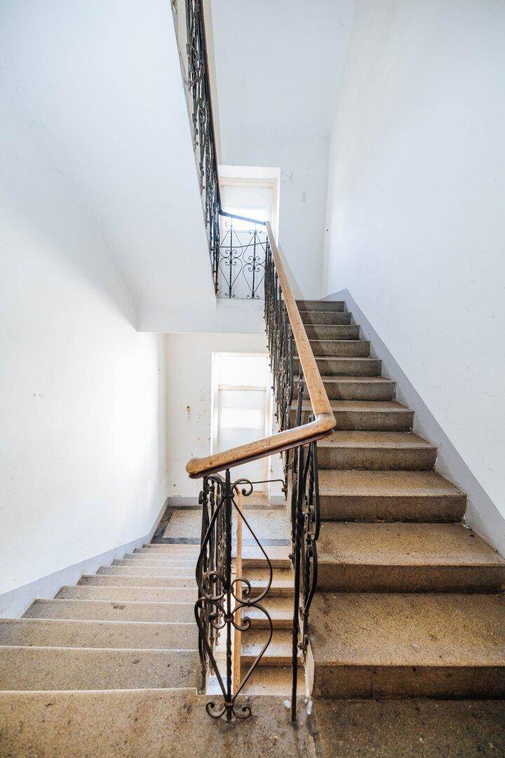 Historisches Treppenhaus mit Steinstufen und schmiedeeisernem Geländer in einem Altbau.