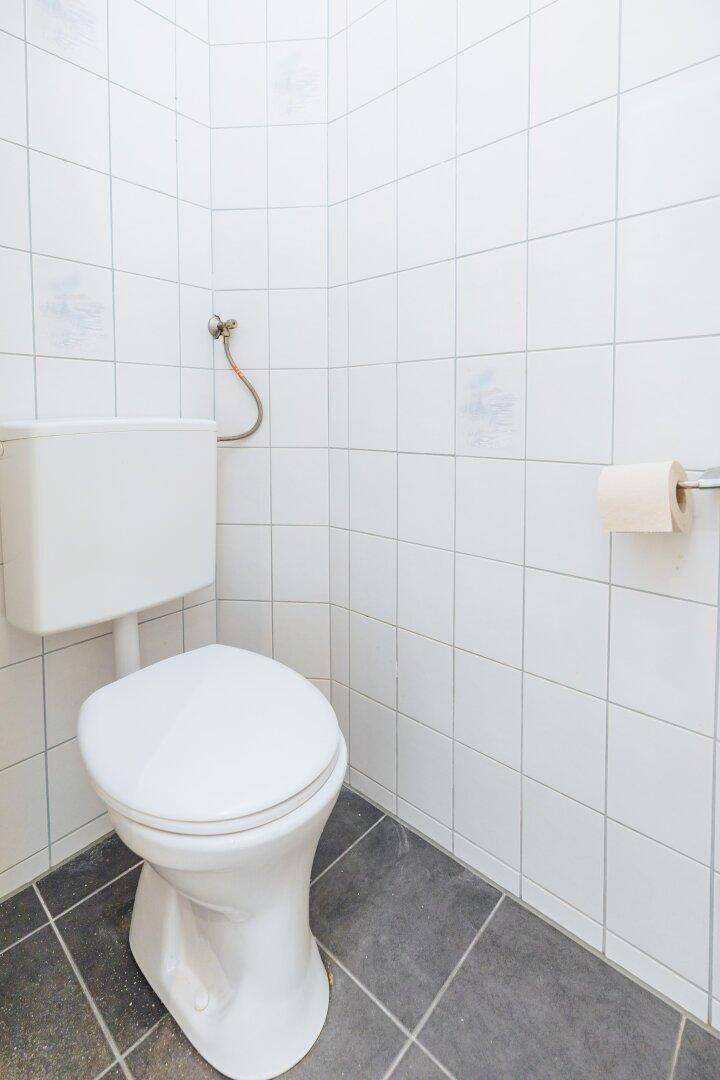 Kleines WC mit weißen Wandfliesen, dunklem Boden und einer Standardtoilette.