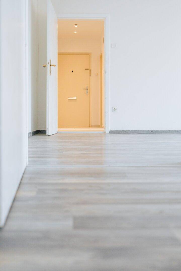 Detailansicht des Laminatbodens in einem hellen Flur mit offener Tür zu einem weiteren Raum.