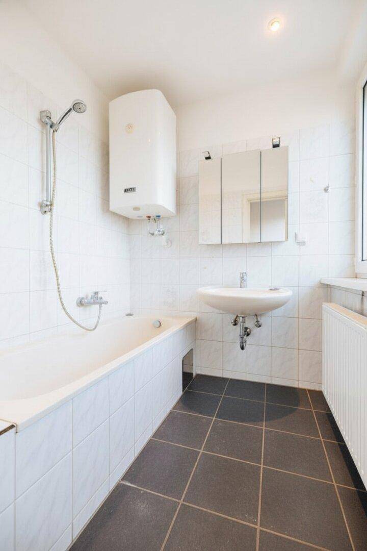 Helles Badezimmer mit Badewanne, Dusche, Waschbecken und einem Fenster für gute Belüftung.