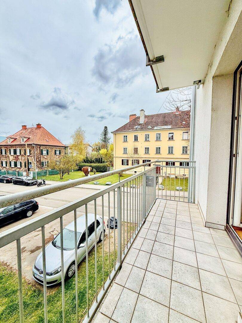 Balkon mit Fliesenboden und Blick auf die Straße und die gegenüberliegenden Gebäude.