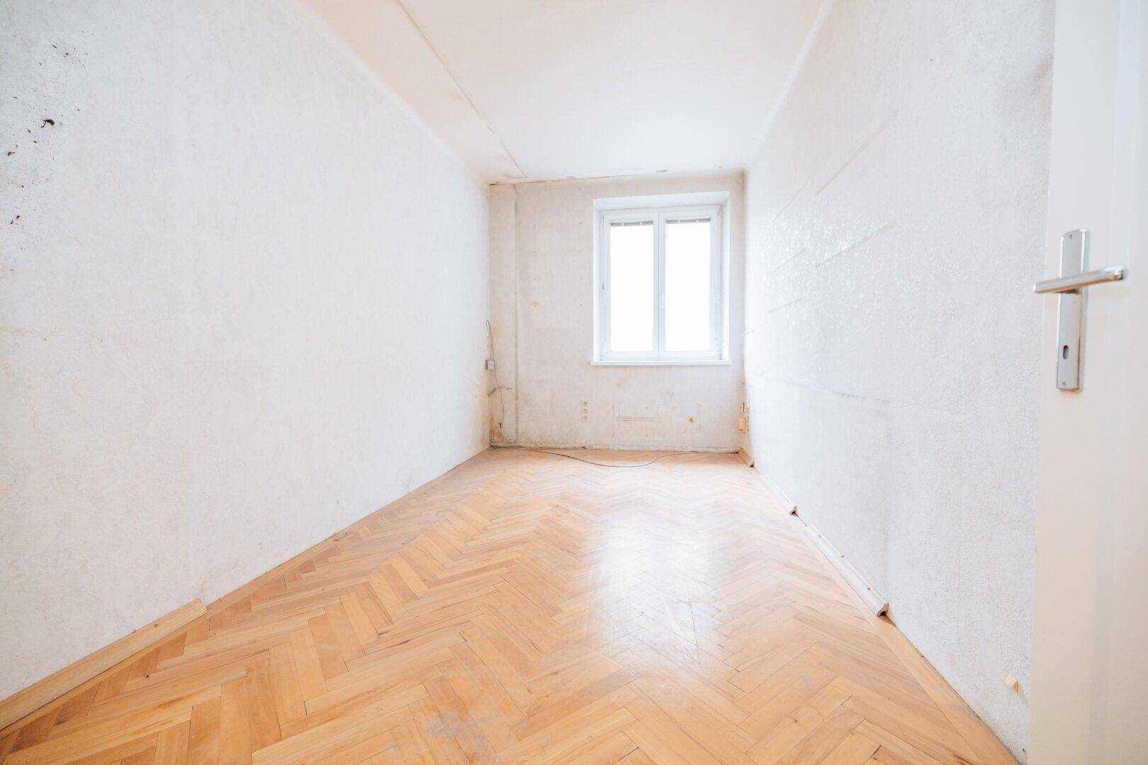 Helles, leeres Zimmer mit Fischgrätparkettboden und einem Fenster, ideal für eine Neugestaltung.