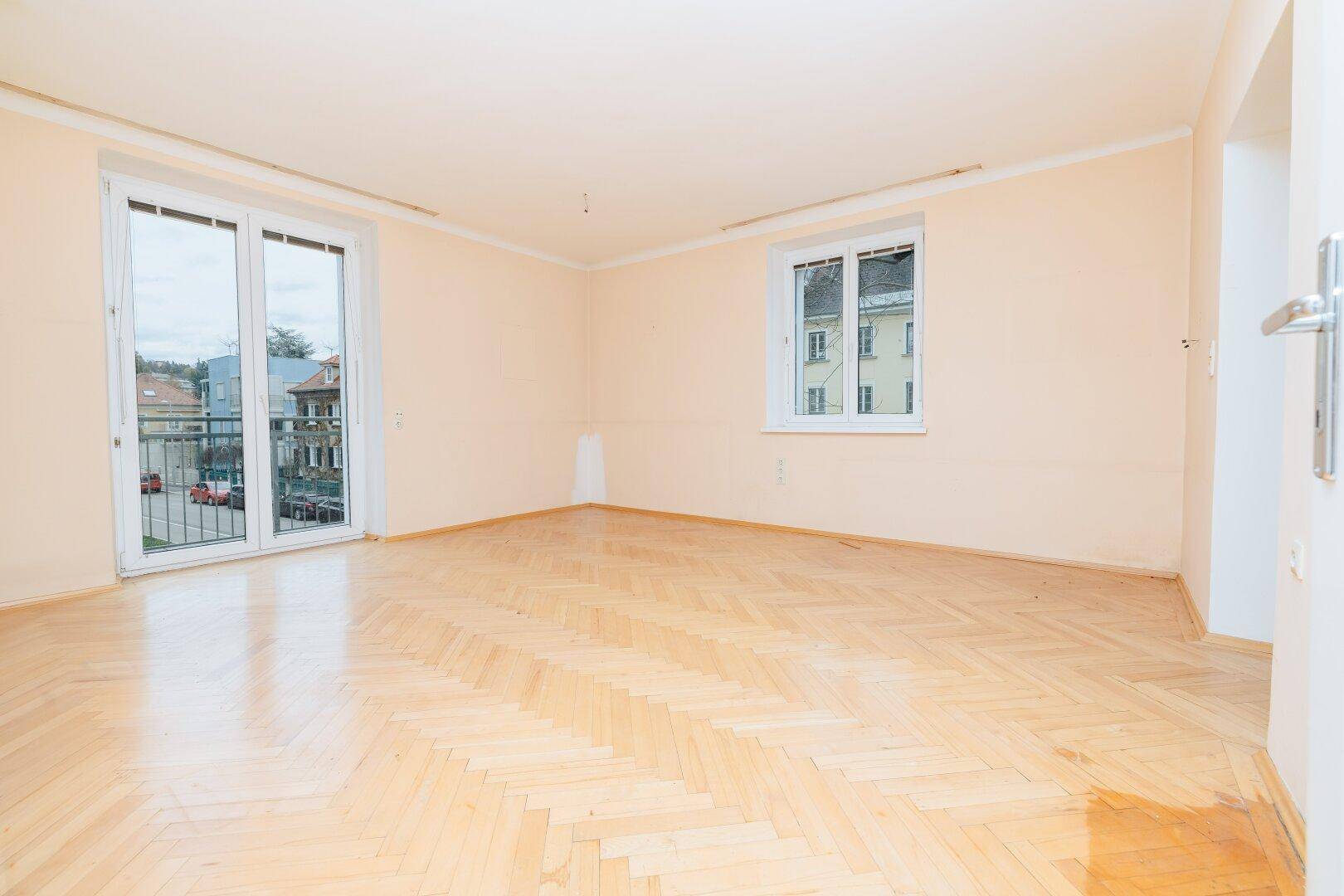 Heller, leerer Raum mit Fischgrätparkettboden und Zugang zu einem Balkon.