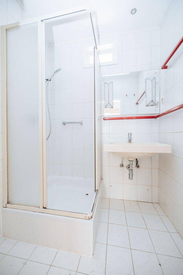 Badezimmer mit Duschkabine, Waschbecken und weißen Fliesen an Wänden und Boden.