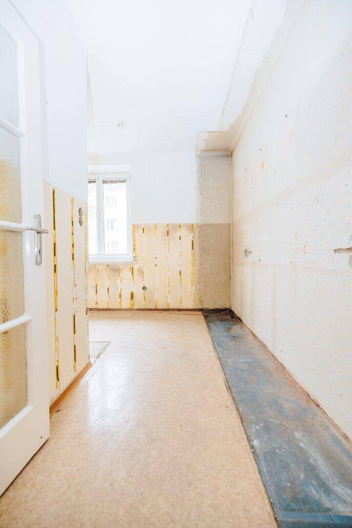 Leerer Küchenraum mit vorbereiteten Anschlüssen und Fenster, bereit für den Einbau einer neuen Küche.