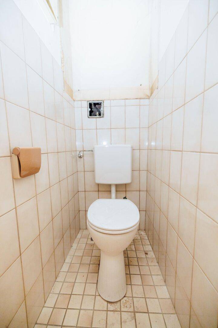 Separate Toilette mit WC und hellen Fliesen an Wänden und Boden.