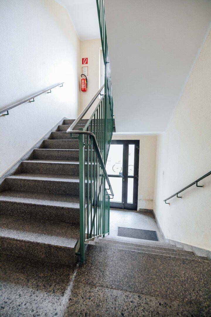 Treppenhaus mit Steinstufen und Metallgeländer in einem Mehrfamilienhaus.