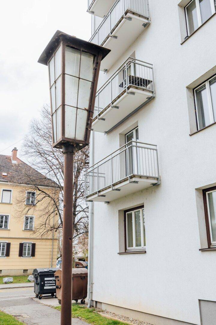 Weiße Gebäudefassade mit mehreren Balkonen und einer alten Straßenlaterne im Vordergrund.