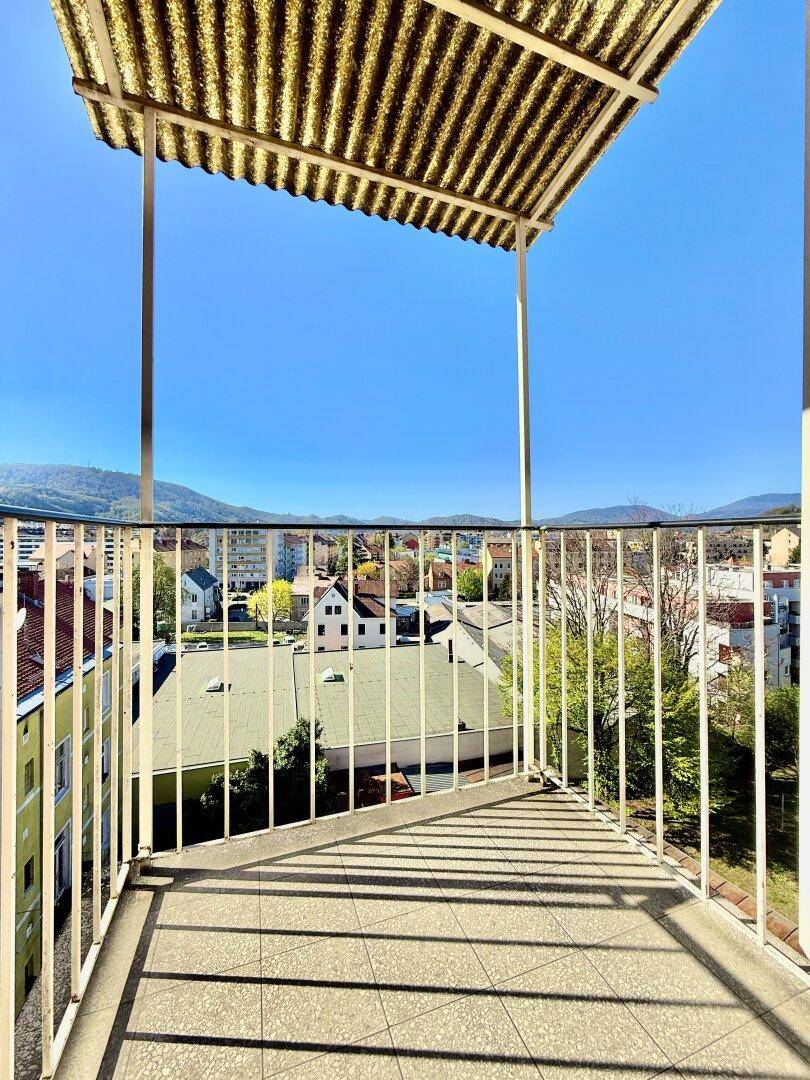 Sonniger Balkon mit Fliesenboden und Überdachung, bietet einen weiten Blick über die Stadt und auf die Berge.