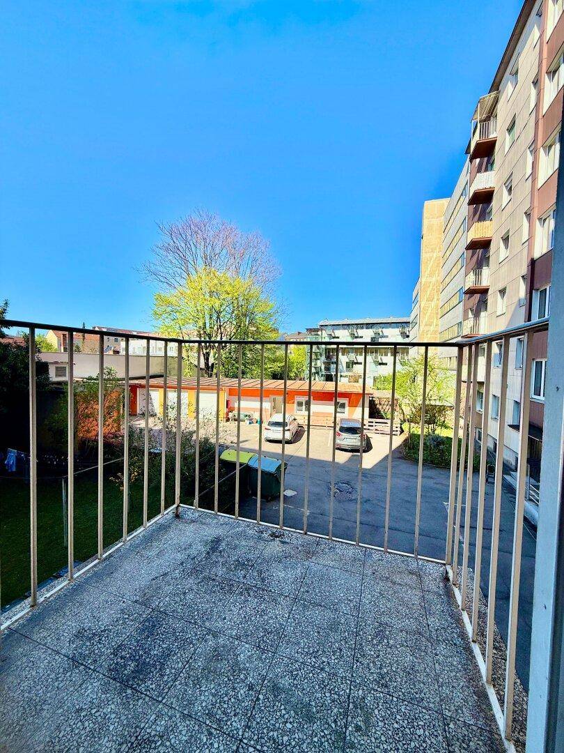 Balkon mit gefliestem Boden und Metallgeländer, bietet einen Blick auf den Innenhof und umliegende Gebäude.