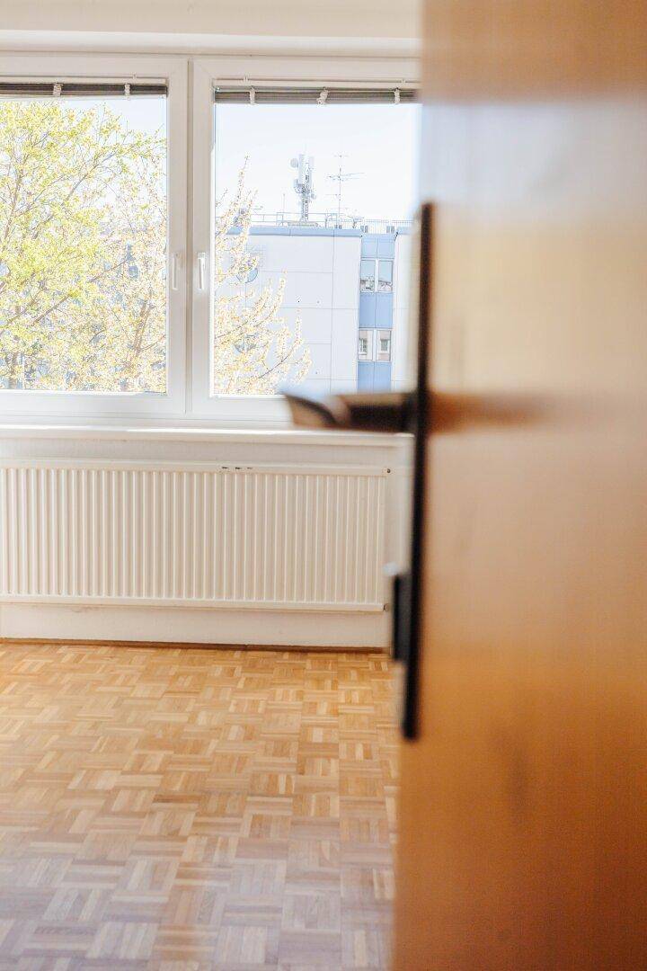 Detailansicht eines Fensters mit Heizkörper und Parkettboden in einem hellen Raum.