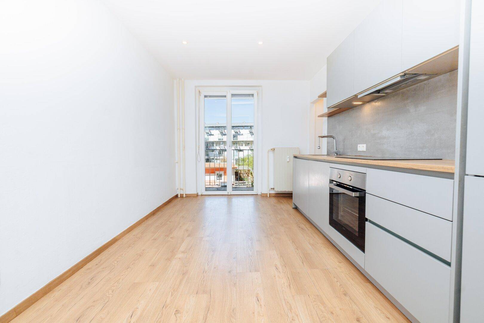 Moderne Küche mit grauen Schränken und Zugang zu einem französischen Balkon mit Stadtblick.