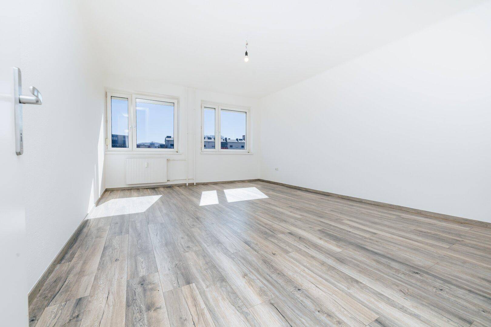 Geräumiges, unmöbliertes Zimmer mit hellem Laminatboden und großen Fenstern für natürliche Belichtung.