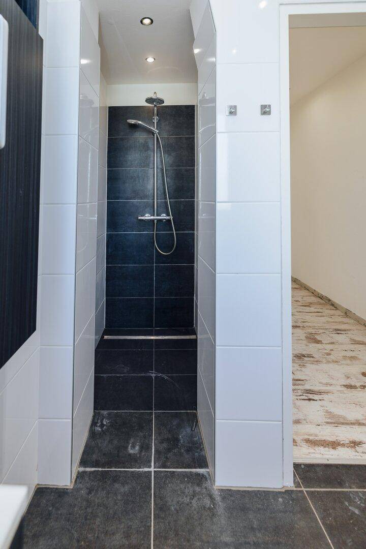 Duschbereich in einem modernen Badezimmer mit dunklen Wandfliesen und weißer Umrandung.