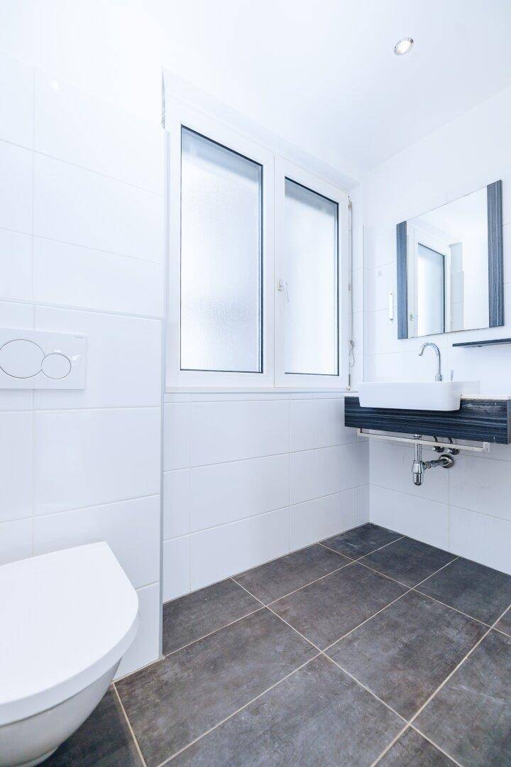 Helles Badezimmer mit Fenster, wandhängendem WC und modernem Waschtisch mit Spiegel.