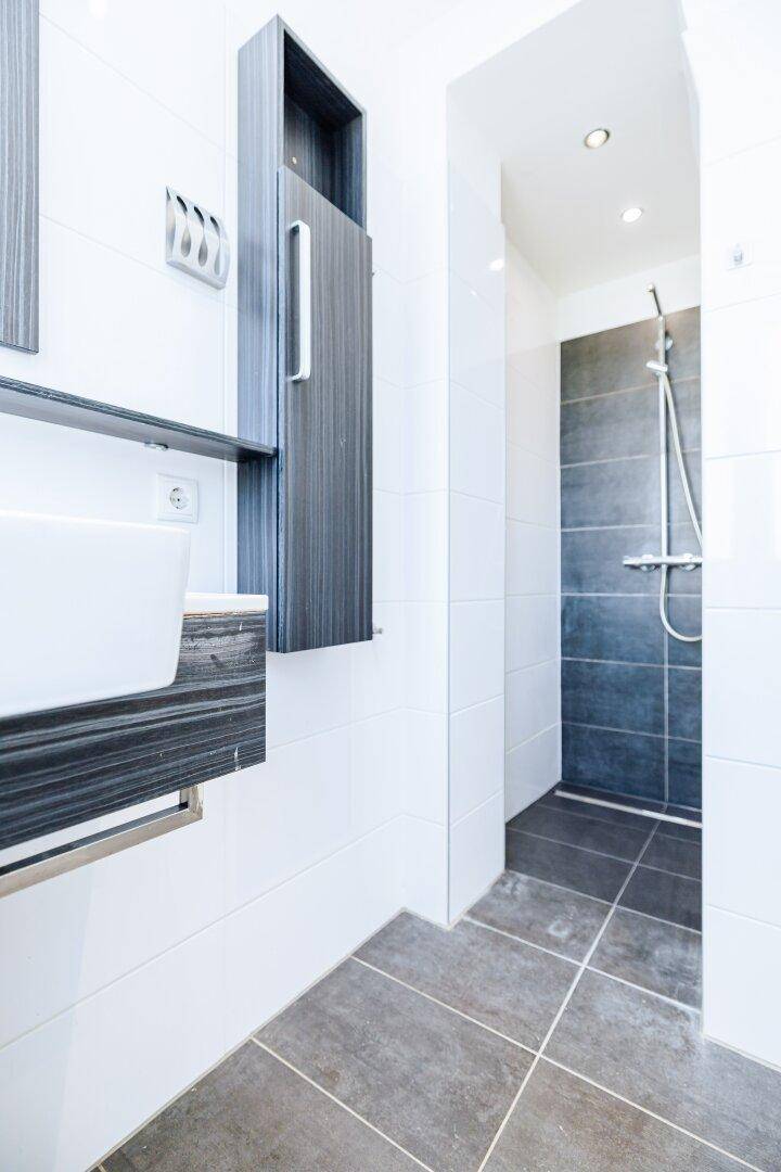 Modernes Badezimmer mit weiß-grauen Fliesen, Waschtisch und einer begehbaren Dusche.
