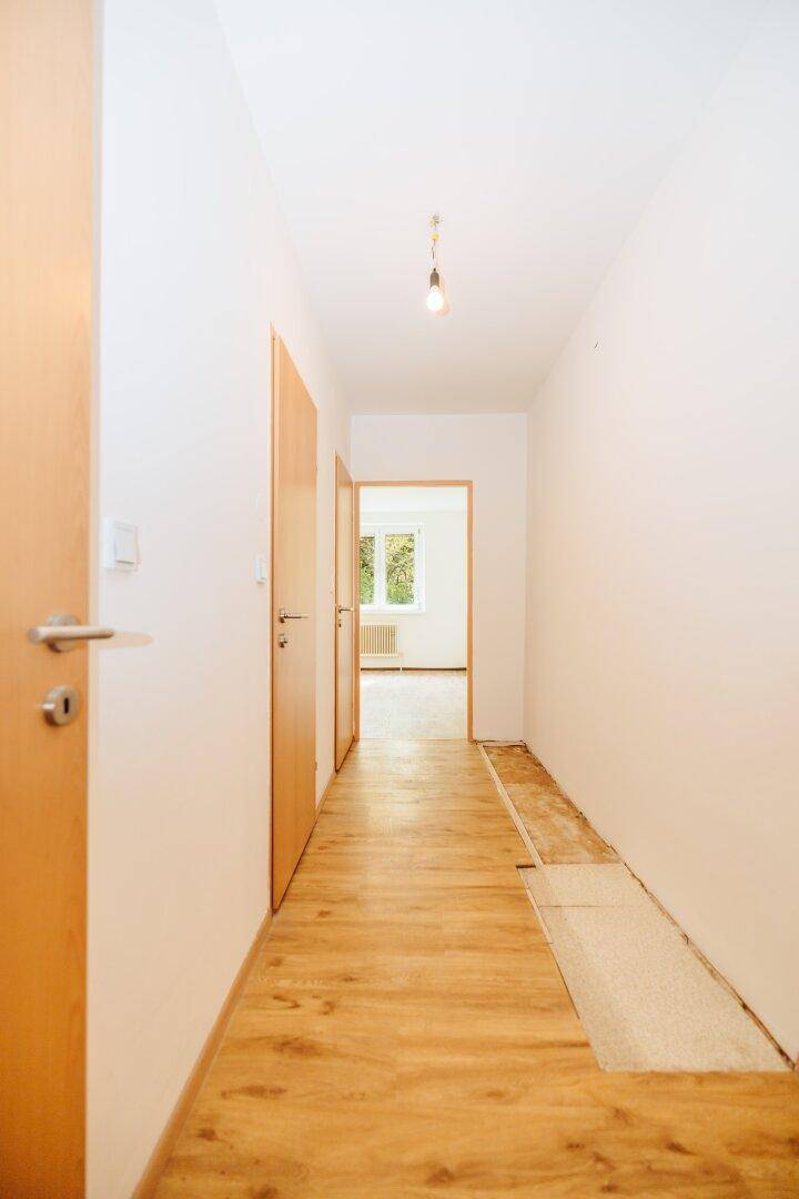 Heller Flur mit Laminatboden und Blick in einen angrenzenden Raum mit Fenster.