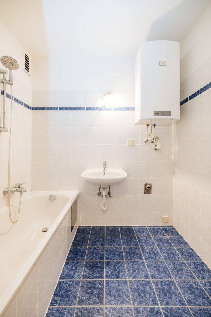 Gefliestes Badezimmer mit Badewanne, Waschbecken und einem Warmwasserboiler an der Wand.