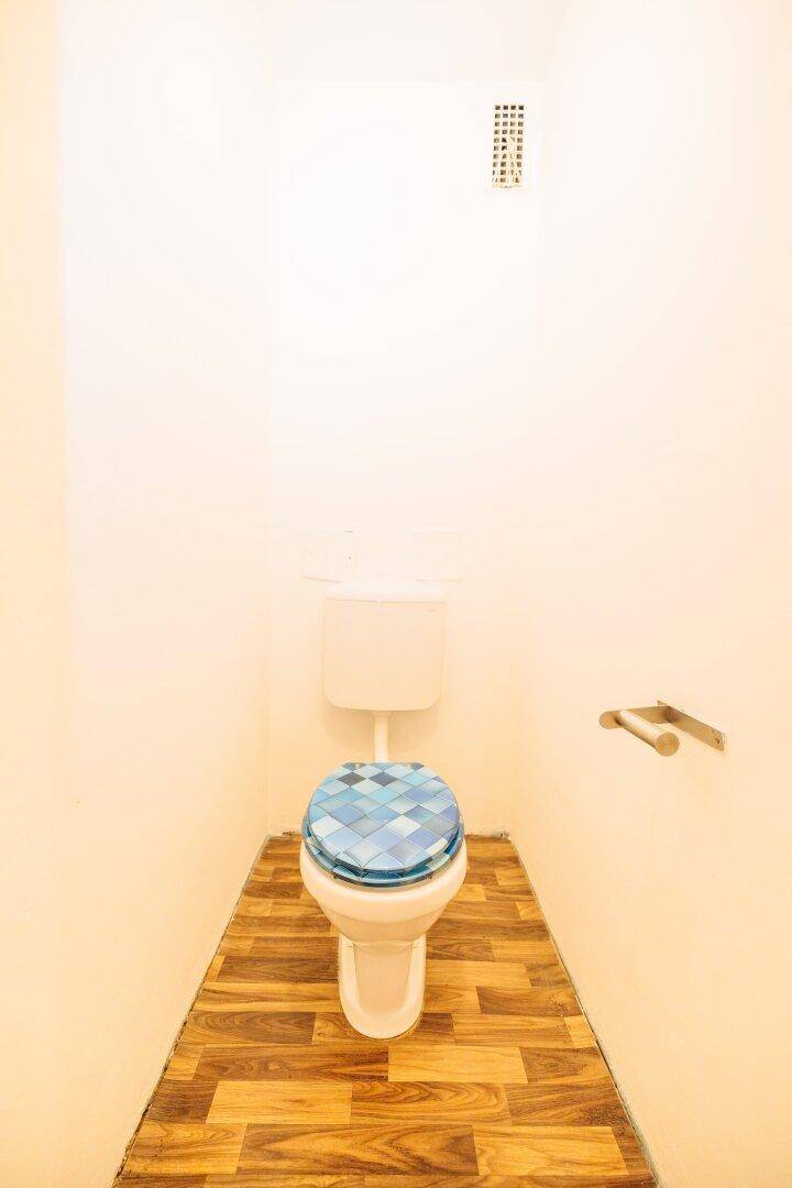 Separate Toilette mit WC, kleinem Waschbecken und Holzbodenoptik.