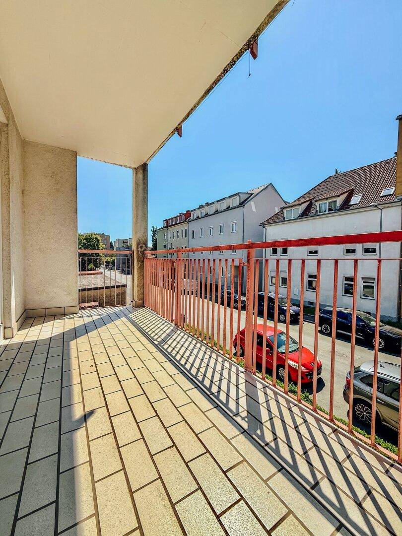 Sonniger Balkon mit hellen Fliesen und rotem Metallgeländer, ideal für entspannte Momente im Freien.