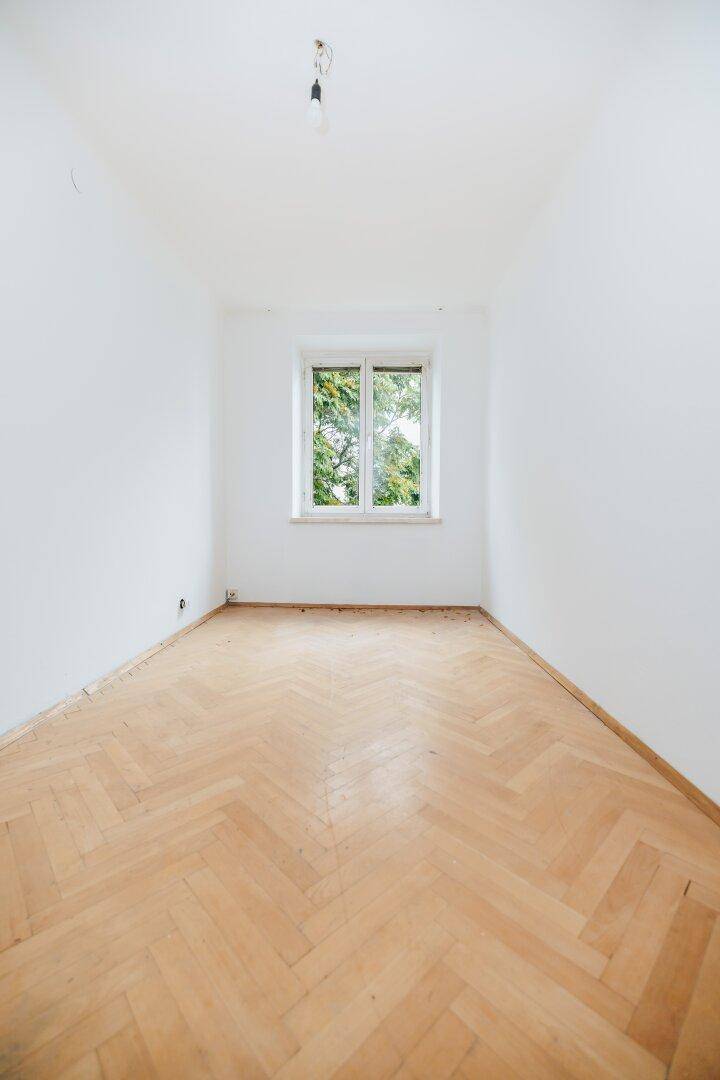 Leeres Zimmer mit Fischgrätparkettboden und einem Fenster, das viel Tageslicht hereinlässt.
