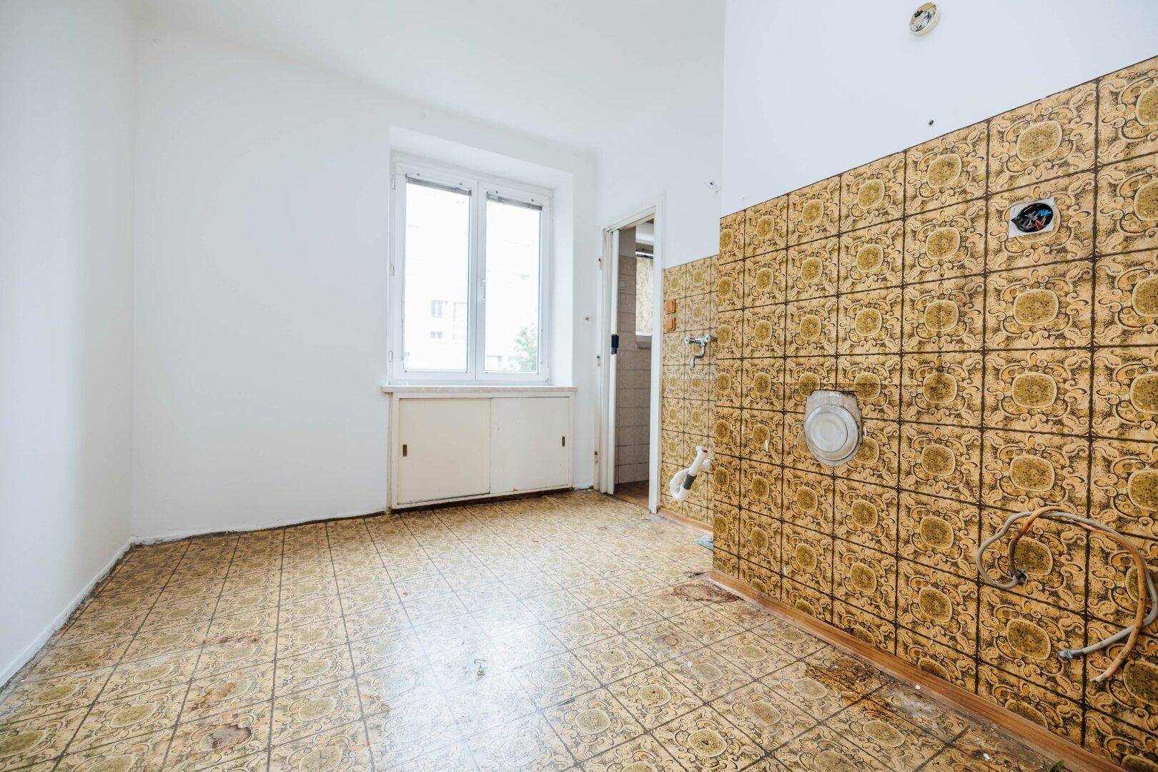 Leere Küche mit älteren Fliesen an Wand und Boden, bereit für eine Renovierung.