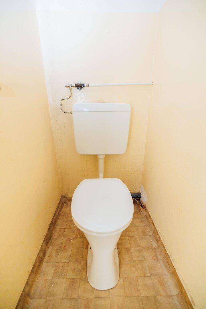 Separate Toilette mit gelben Wänden und gefliestem Boden, in einfachem, funktionalem Zustand.