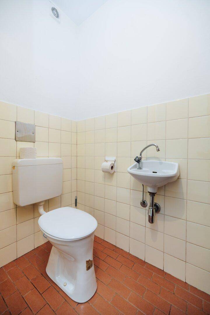 Separates WC mit hellgelben Fliesen, Toilette und kleinem Handwaschbecken.