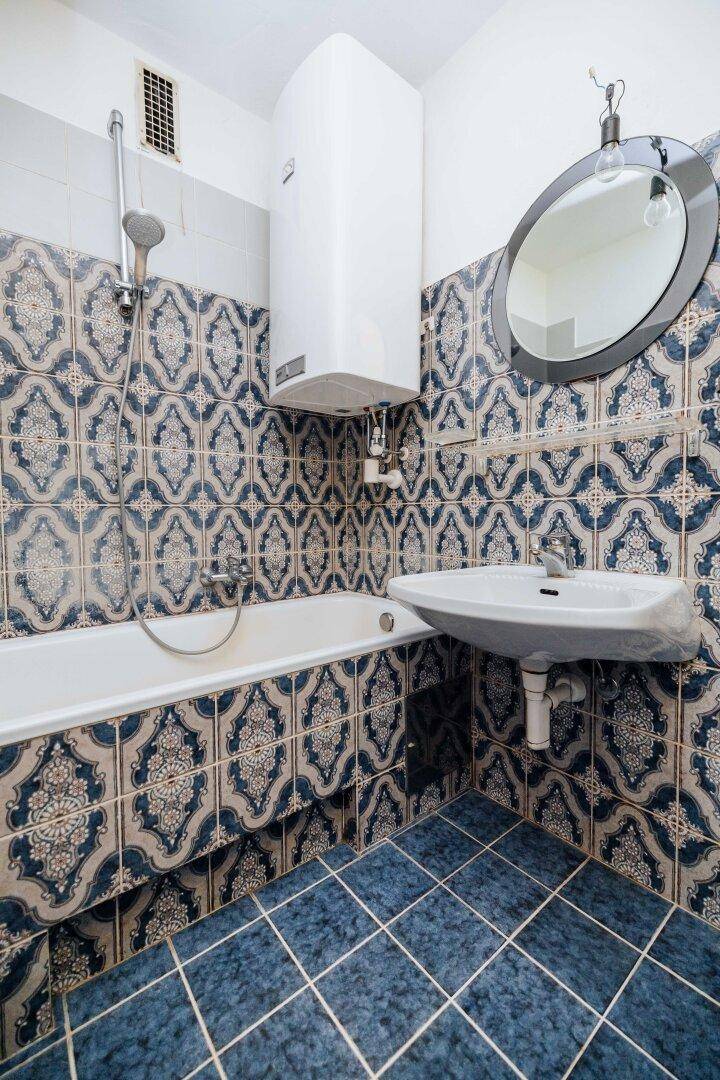Badezimmer mit blauen, gemusterten Fliesen, Badewanne mit Duschfunktion und Waschbecken.