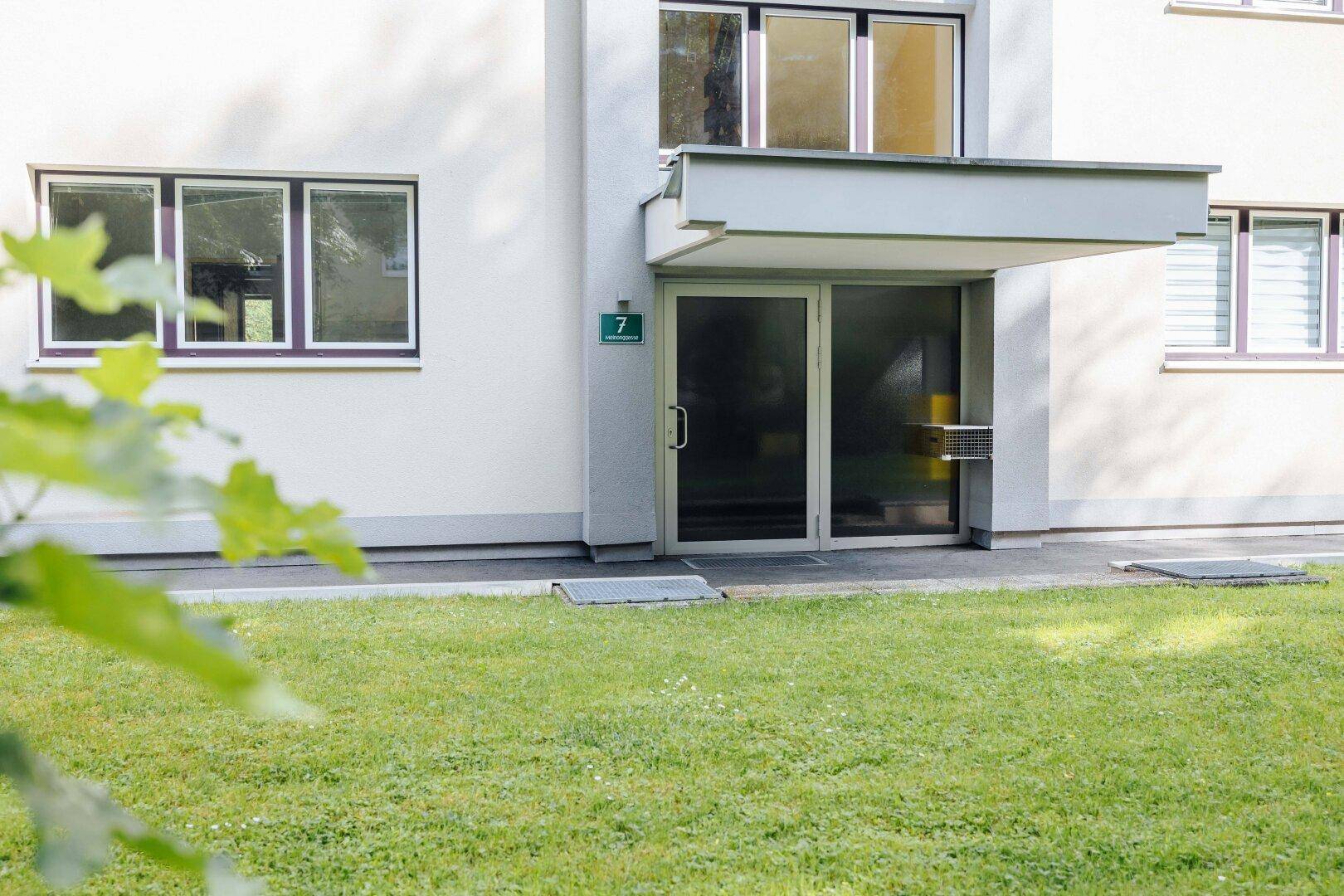Eingangsbereich eines Mehrfamilienhauses mit gepflegtem Rasen und moderner Tür.