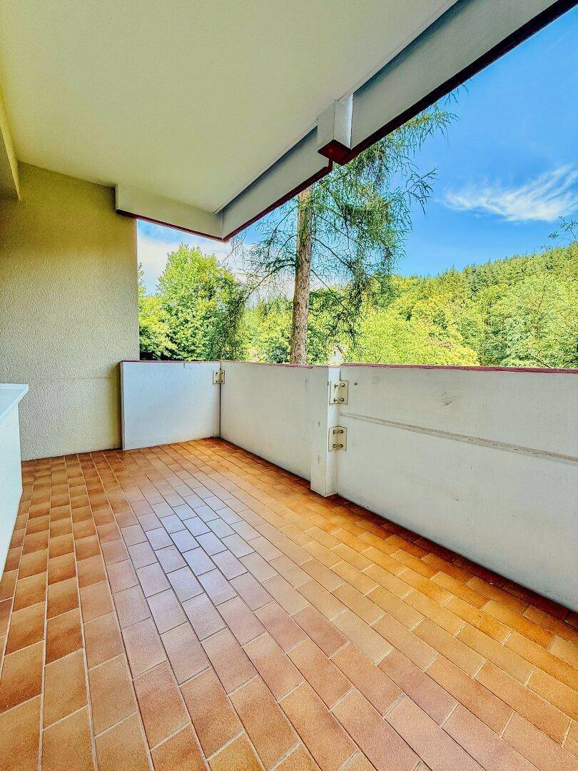 Heller Balkon mit Fliesenboden und weitem Blick auf die umliegende grüne Landschaft.