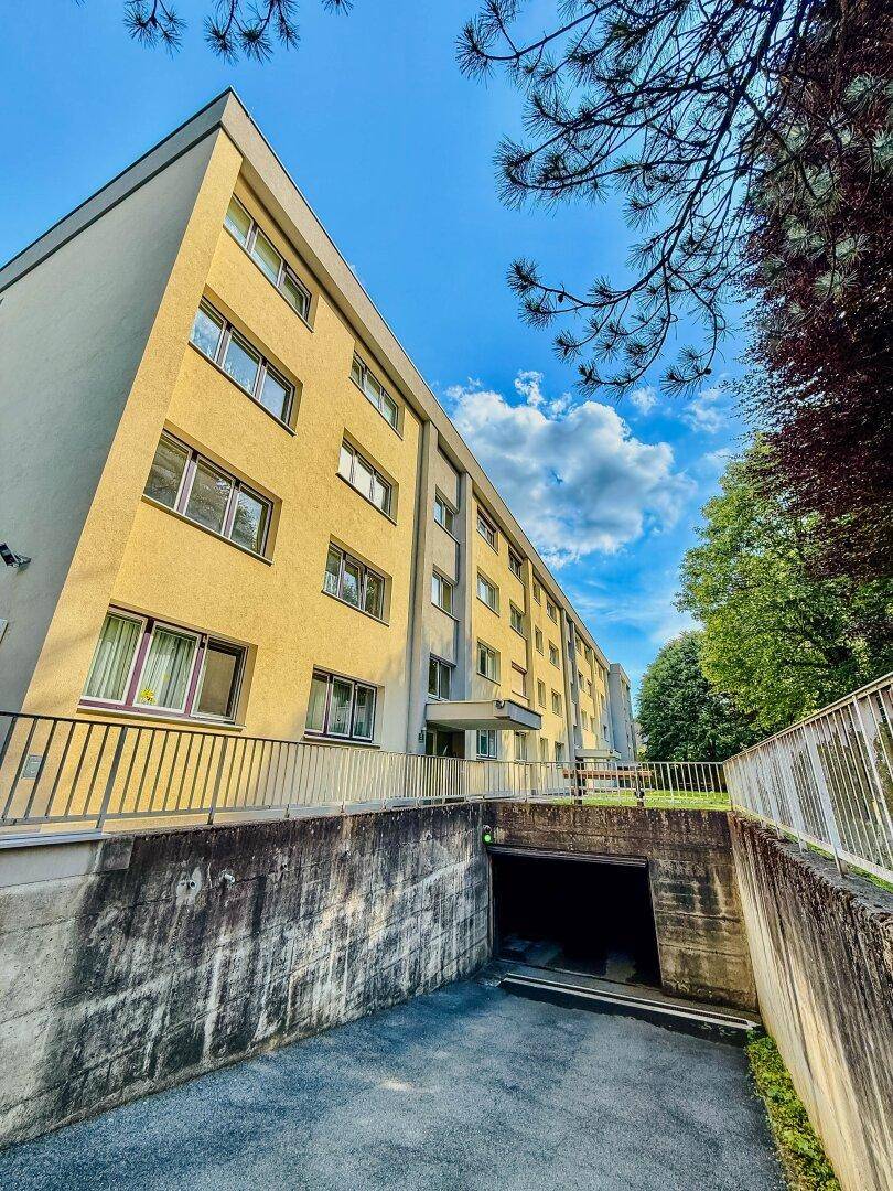 Mehrstöckiges Gebäude mit gelber Fassade und Zufahrt zu einer Tiefgarage.
