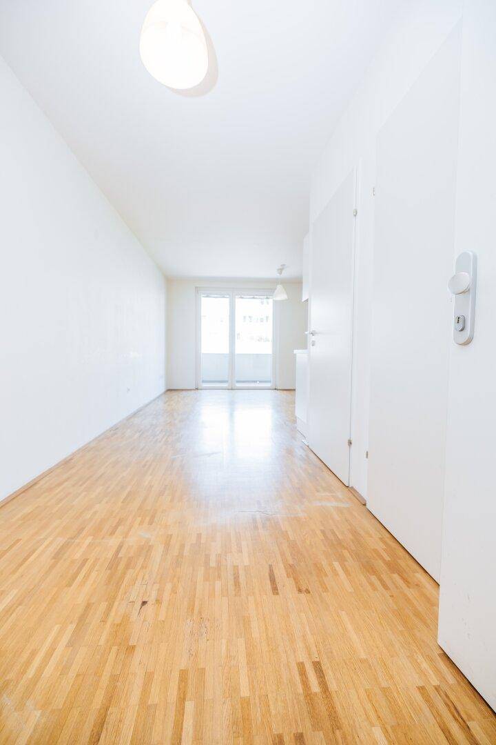 Langer, heller Flur mit Parkettboden, der zu einem Zimmer mit Balkonzugang führt.