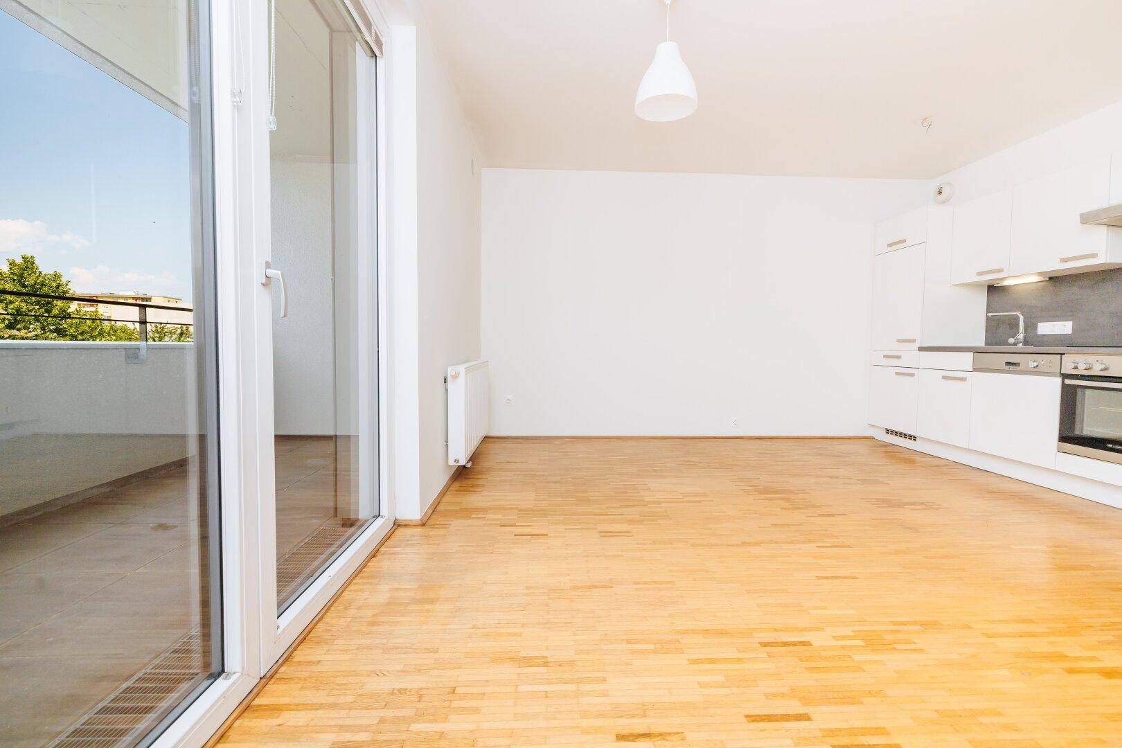 Geräumiger, heller Wohnbereich mit Parkettboden und offener Küchenzeile, bereit zur Einrichtung.