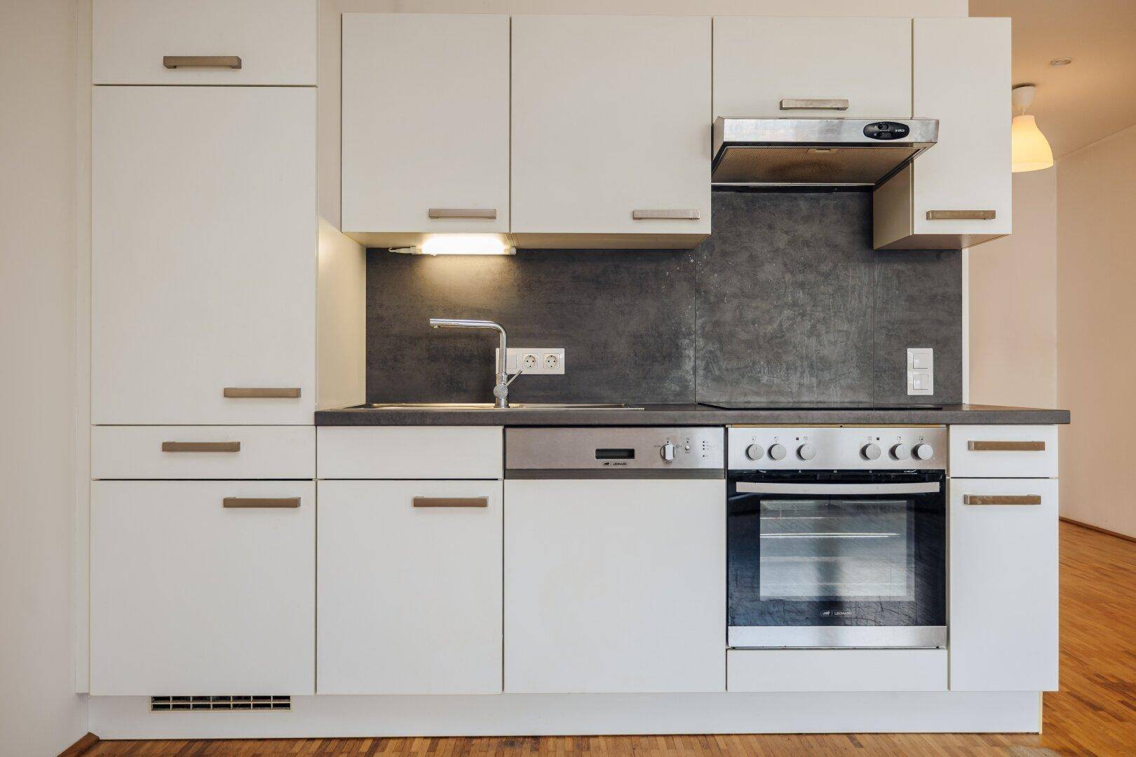 Moderne Einbauküche mit weißen Schränken, integrierten Geräten und Dunstabzugshaube.
