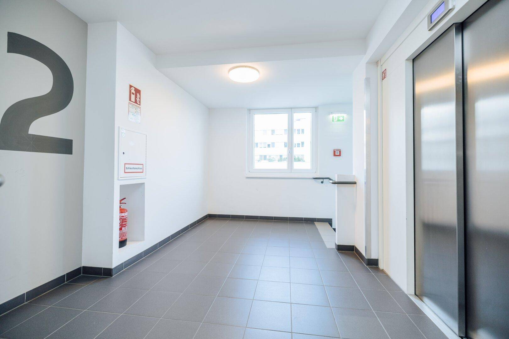 Heller Flur im zweiten Stock eines Gebäudes mit Aufzug und Fliesenboden.