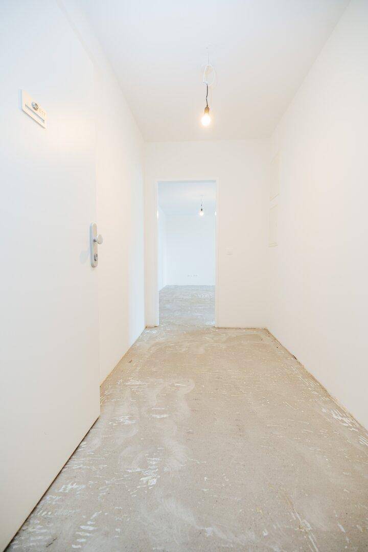 Heller Flur mit weiß gestrichenen Wänden und Betonboden, der zu weiteren Räumen führt.