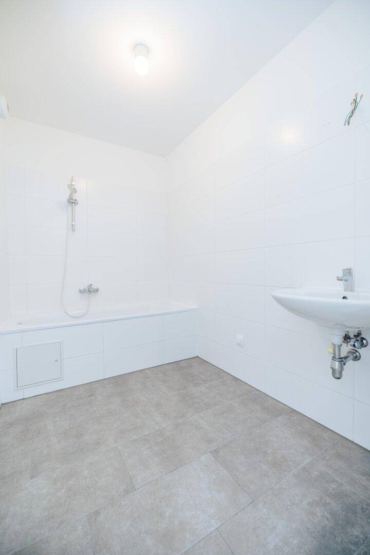 Modernes Badezimmer mit weißen Fliesen, grauen Bodenfliesen, Badewanne und Waschbecken.