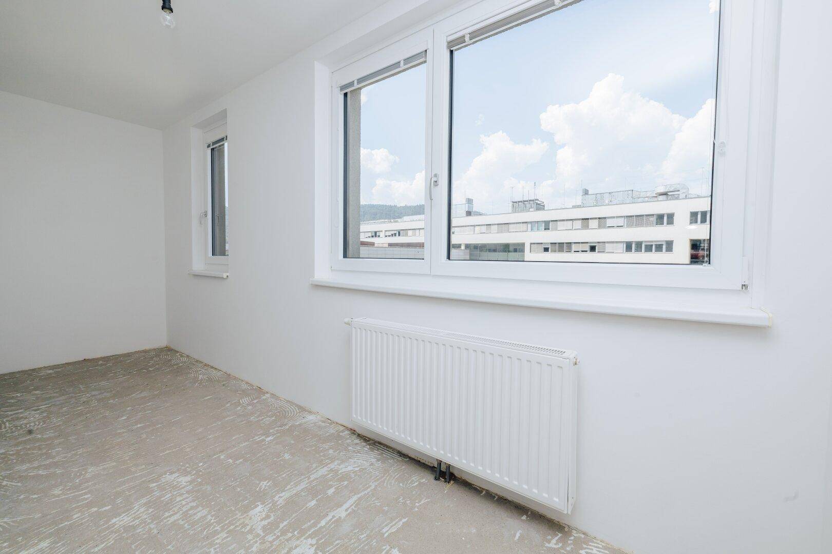 Großes Fenster in einem hellen Raum mit Blick auf die umliegenden Gebäude.
