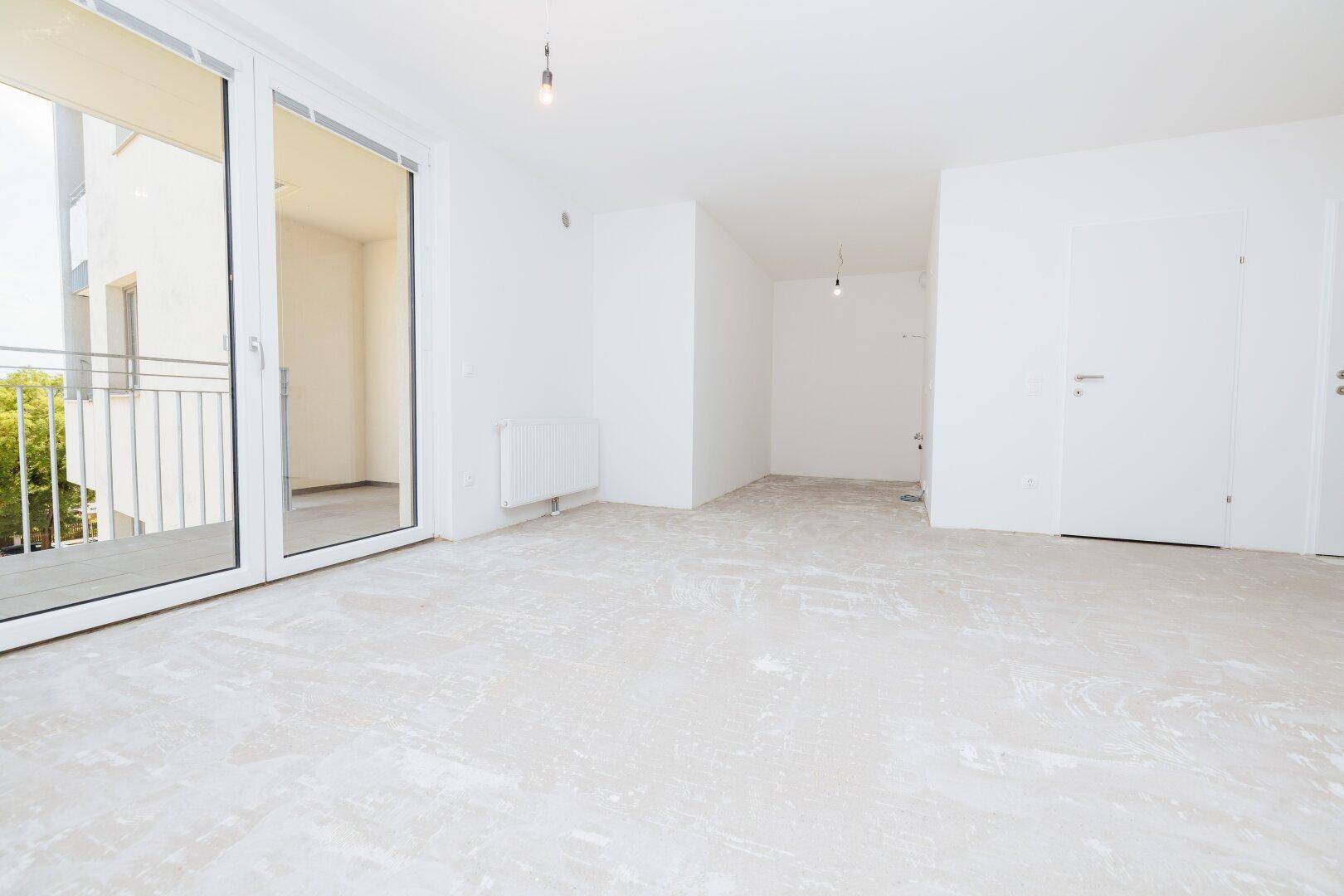 Heller, unmöblierter Raum mit weiß gestrichenen Wänden und Zugang zu einem Balkon.
