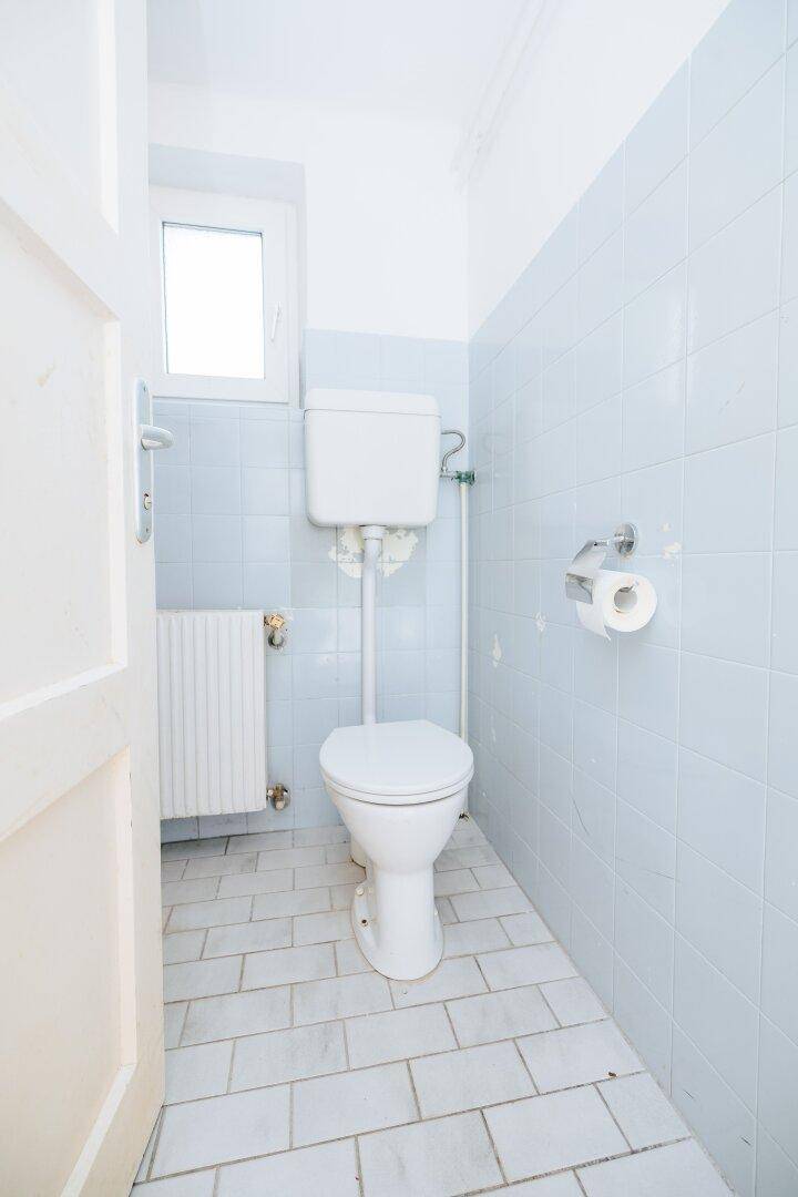 Kleines WC mit hellblauen Fliesen, Toilette und einem Fenster für natürliche Belüftung.