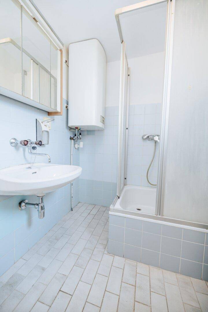 Badezimmer mit hellblauen Fliesen, Waschbecken, Spiegelschrank und einer Duschwanne mit Kabine.