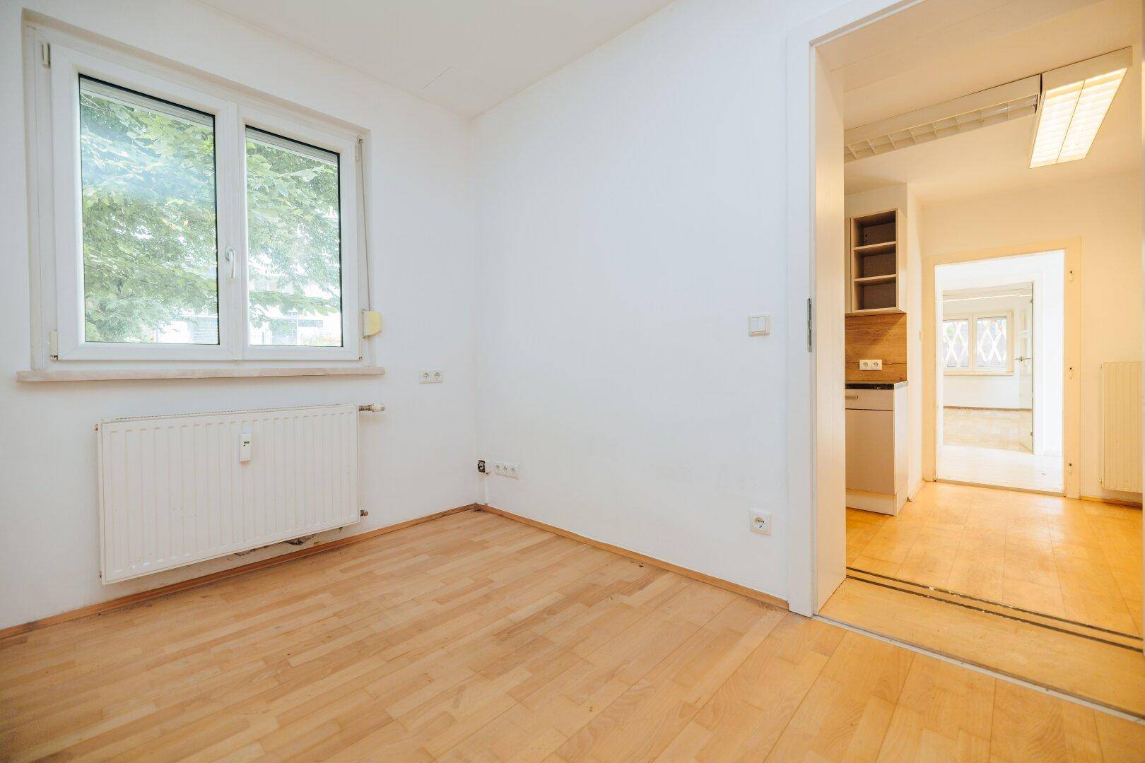 Heller Raum mit Holzboden und Fenster, mit Blick auf einen angrenzenden Bereich der Wohnung.