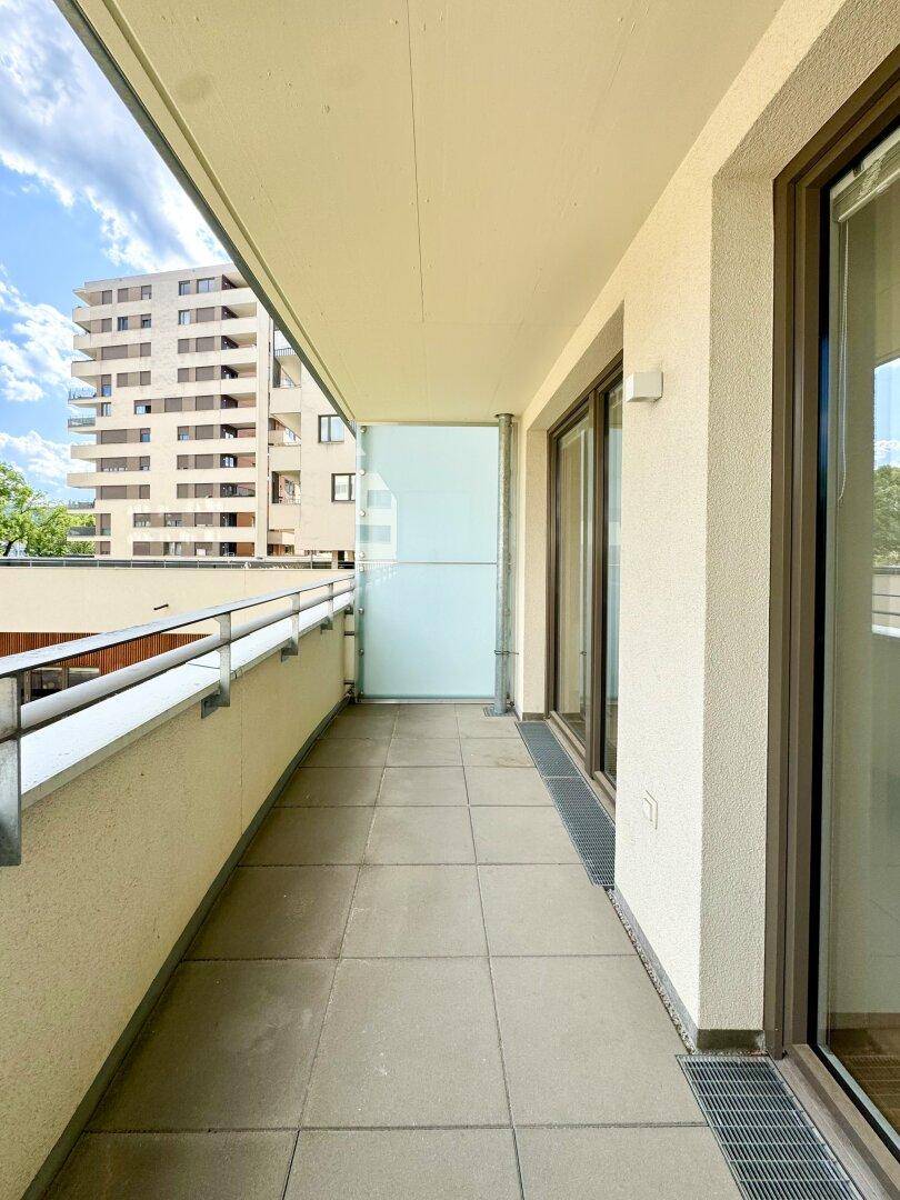 Langer Balkon mit Fliesenboden und Blick auf die umliegenden Gebäude der Wohnanlage.